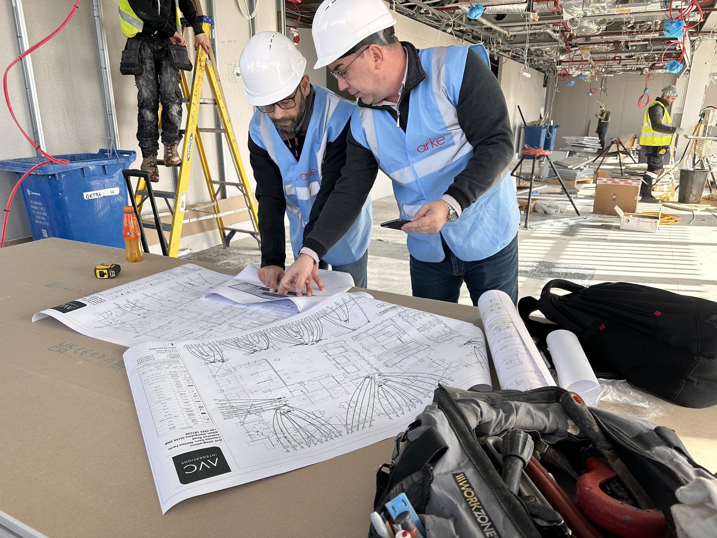 Engineers in hard hats and hi-vis checking a coordinated services drawing on site, with first-fix pipework and containment overhead