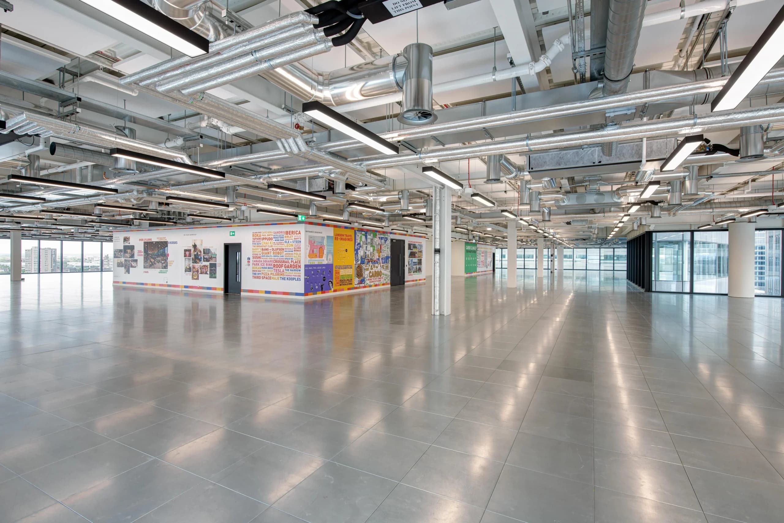 Completed Central London office floor with exposed spiral ductwork, supply and extract terminals and linear lighting coordinated across the soffit