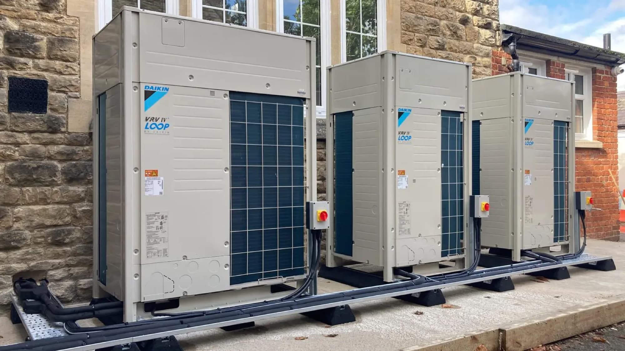 Three Daikin VRV IV outdoor units installed neatly on a concrete base outside a stone building