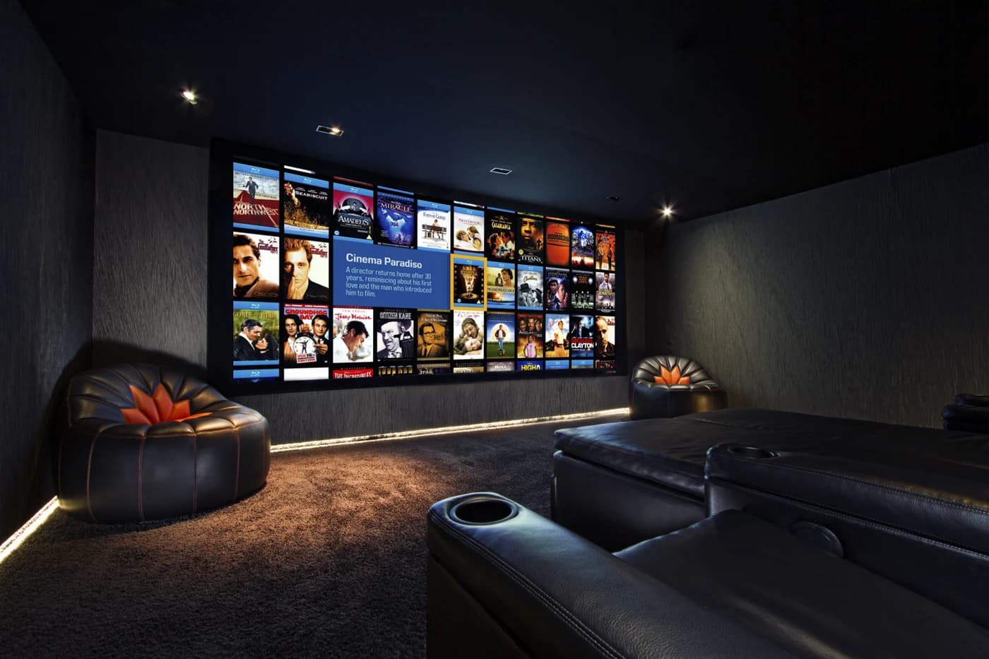 A home cinema room with a large screen showing a film library, tiered leather seating and concealed cove lighting along the walls
