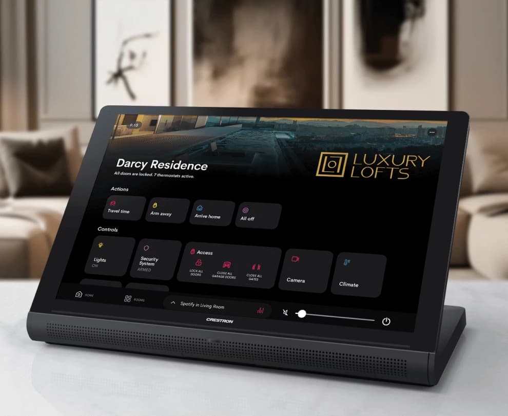 A Crestron Home touch screen on a marble surface in a living room, showing the home view: the residence name, one-touch actions for arriving and leaving, and controls for lights, security, access, cameras and climate